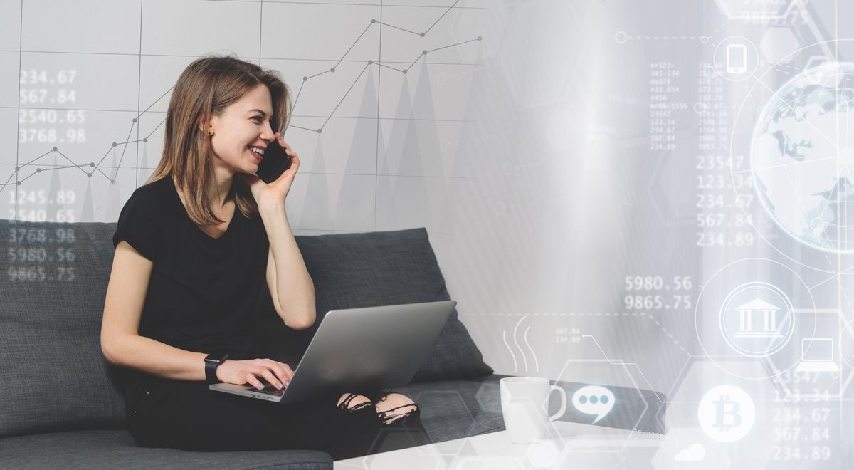 Smiling female freelancer talking phone while working home on her latop sitting on comfortable sofa. Distant job in cozy conditions concept. Copy space for your text.